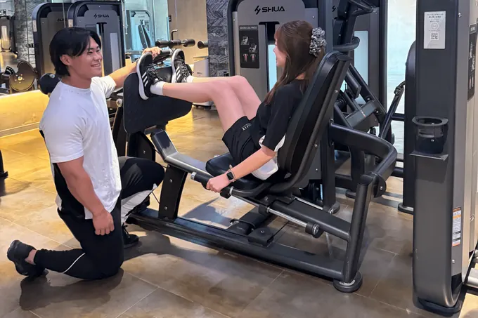 トレーナーのサポートでレッグプレスをする女性